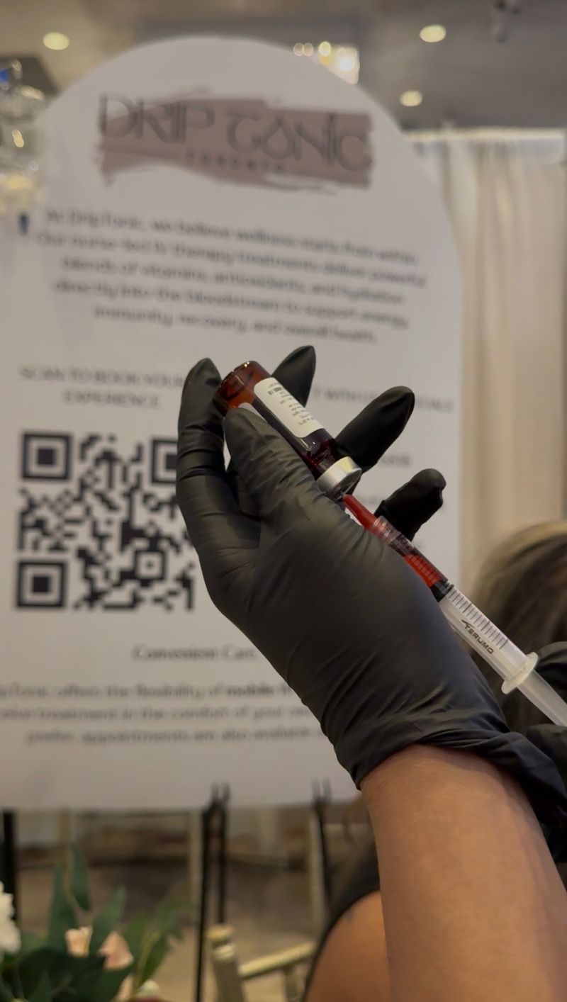 A gloved Drip Tonic RN draws a B12 vitamin shot at the Recharge Bar event station, the Drip Tonic banner behind, at a GTA event.