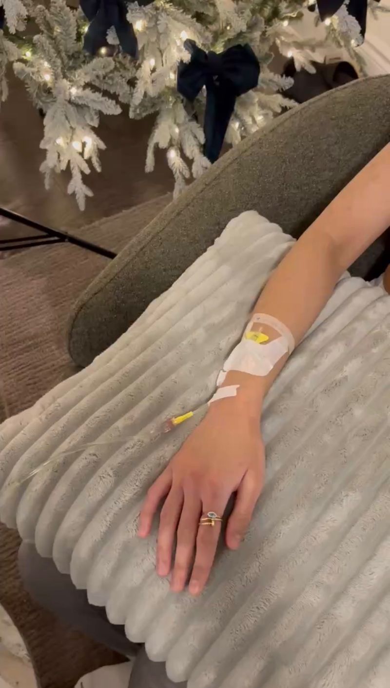 A guest's arm with a taped IV cannula rests on a soft throw beside a flocked white Christmas tree, a Drip Tonic at-home holiday IV drip in the GTA.